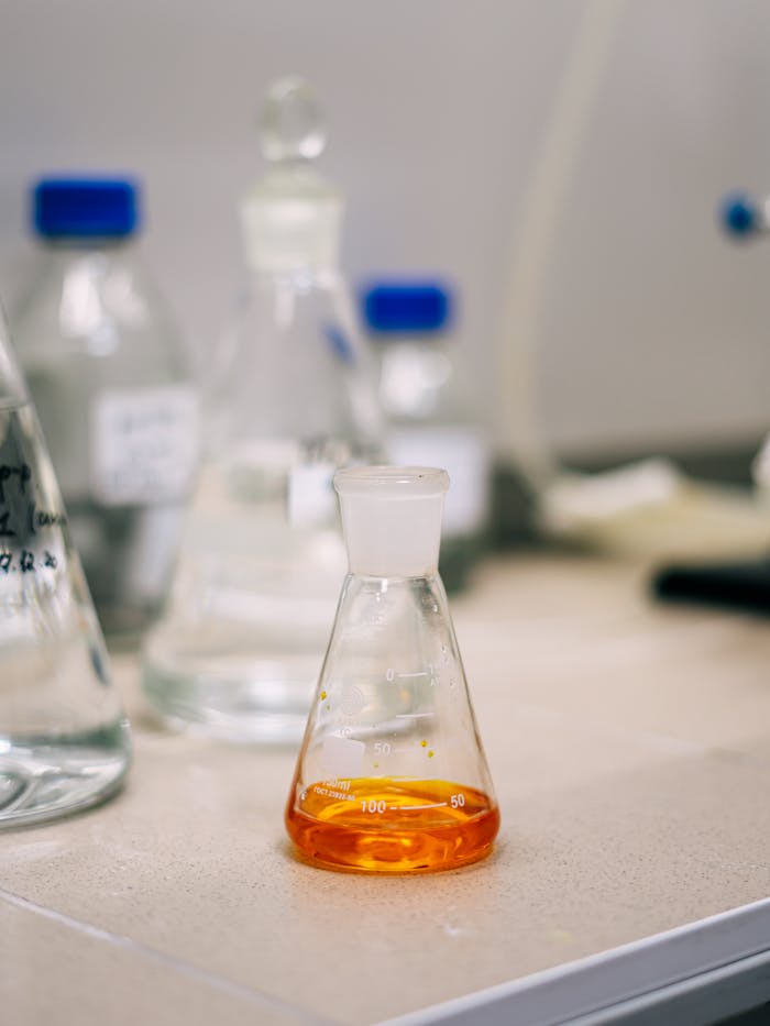 An Erlenmeyer flask containing orange liquid on a lab bench, surrounded by glassware.